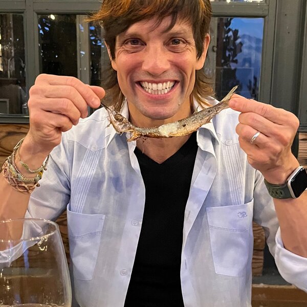 Carli Dávila at a restaurant, smiling with a small fish skeleton held across his face like a grin